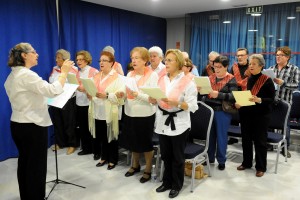 Foto de los participantes en uno de los talleres durante el programa de Vacaciones Sociales. Aparecen en un taller de canto y se muestran leyendo un papel al tiempo que lo recitan