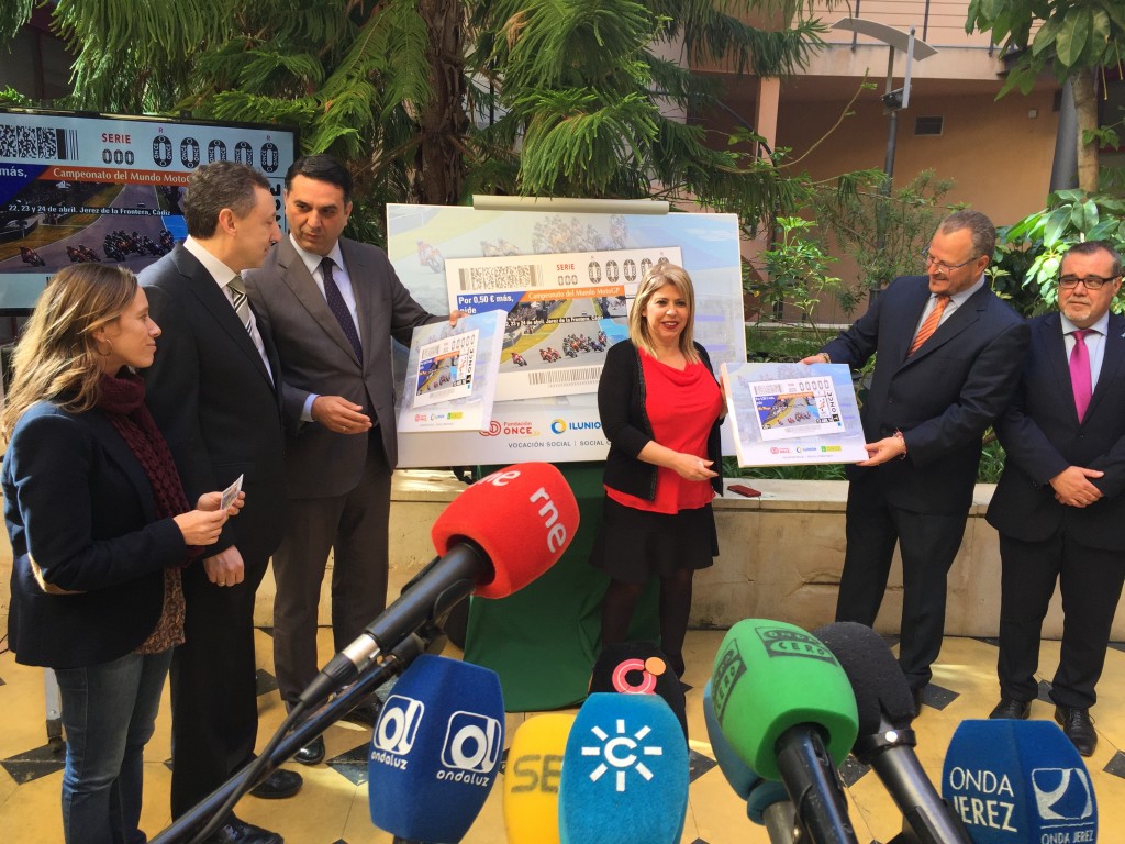 Otra perspectiva de la presentación con los micrófonos de primer plano y las autoridades mostrando el cupón al fondo