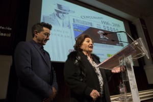 Dolores Abril, viuda de Juanito Valderrama habla en el acto de presentación junto a su hijo y con el cartel del cupón a sus espaldas