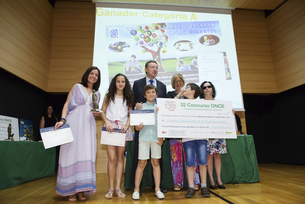 Los alumnos sonrientes muestran desde el escenario sus diplomas