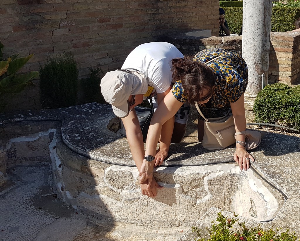 Una profesora guía las manos de un alumno para que vea los restos arqueológicos de Itálica
